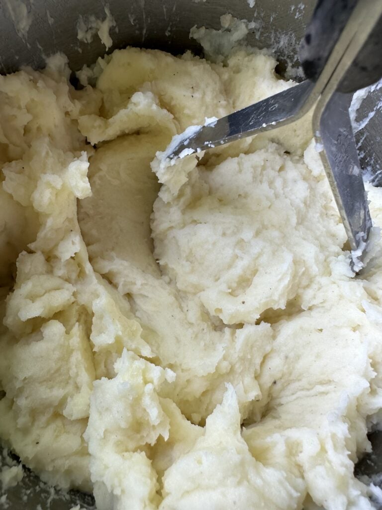Mashed potatoes being mashed with a masher