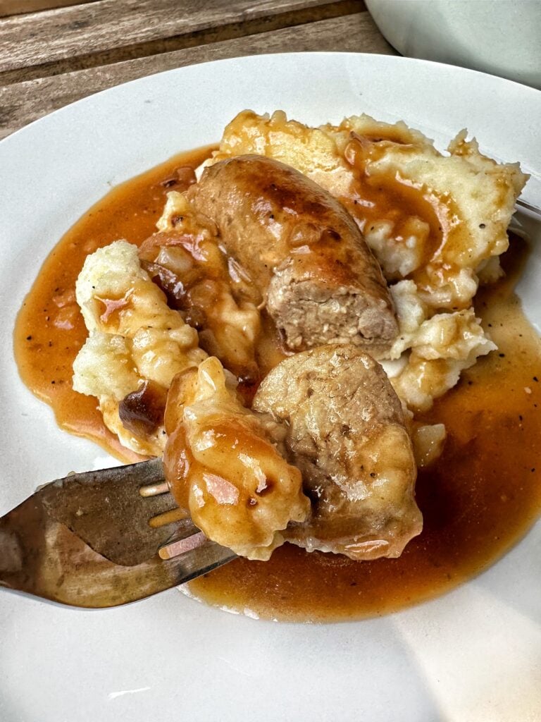 A fork of sausage and mashed potatoes with onion gravy