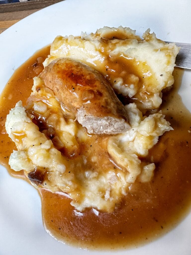 A close up of half a sausage on mashed potatoes covered in gravy