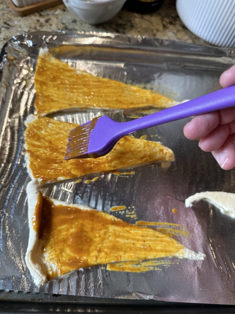 Golden BBQ sauce being spread on to triangles of crescent dough