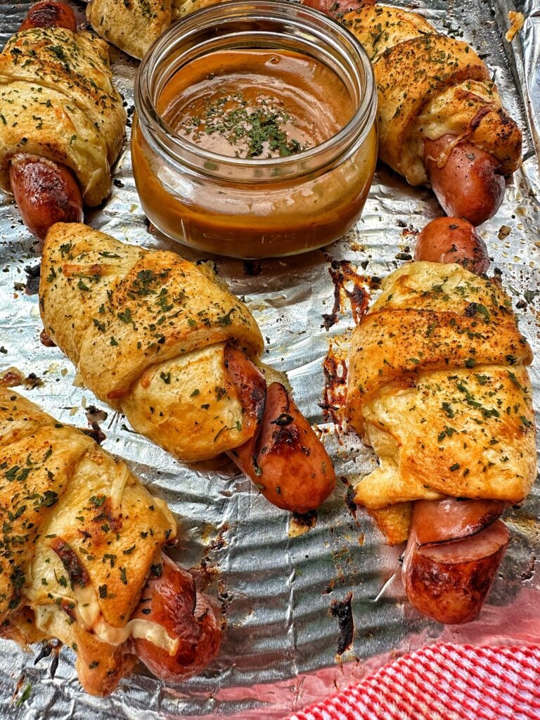 Frank and Swiss bites on a foil baking sheet with a little glass cup of sauce in the middle