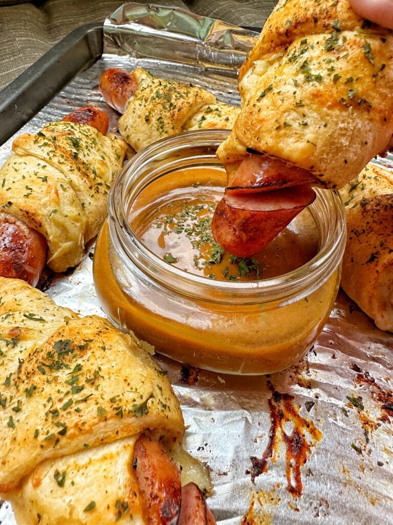 A frank and Swiss bite being dipped into golden BBQ sauce