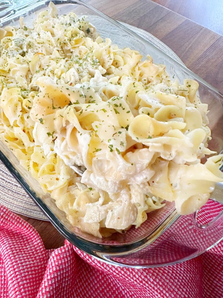 A scoop of baked noodles being taken from a glass baking dish