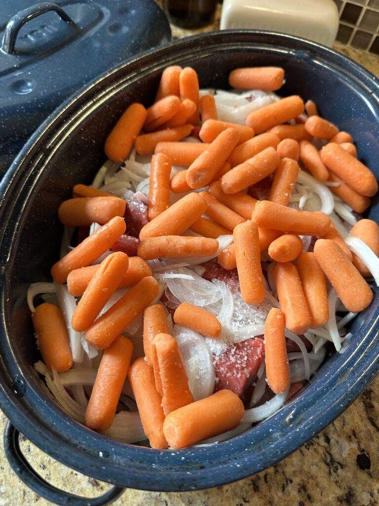 Baby carrots on top of onions and salt and raw beef
