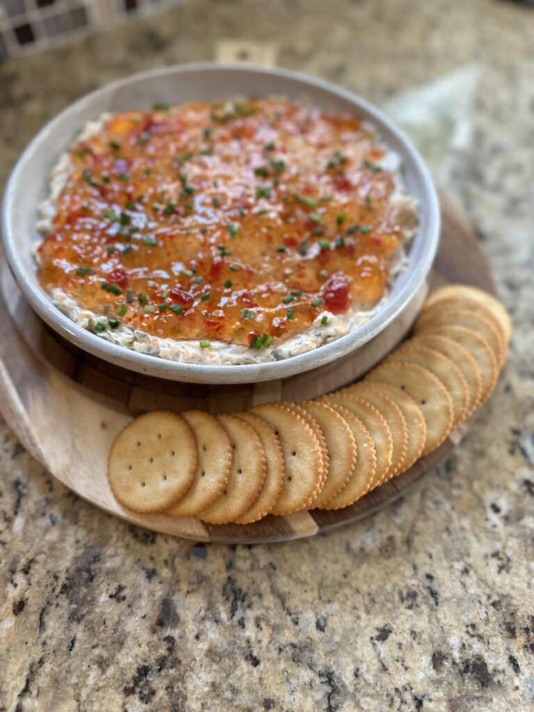 Crackers placed along the side of a bowl of pepper jelly cheese dip