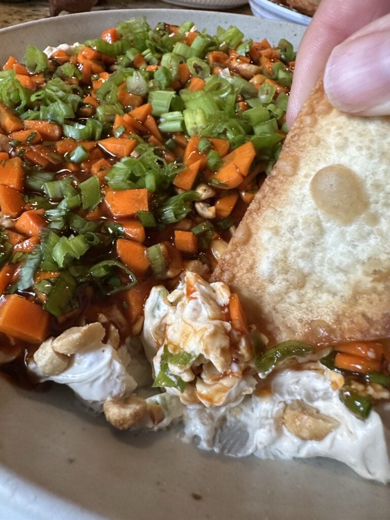 A close up of a won ton chip being dipped into egg roll dip