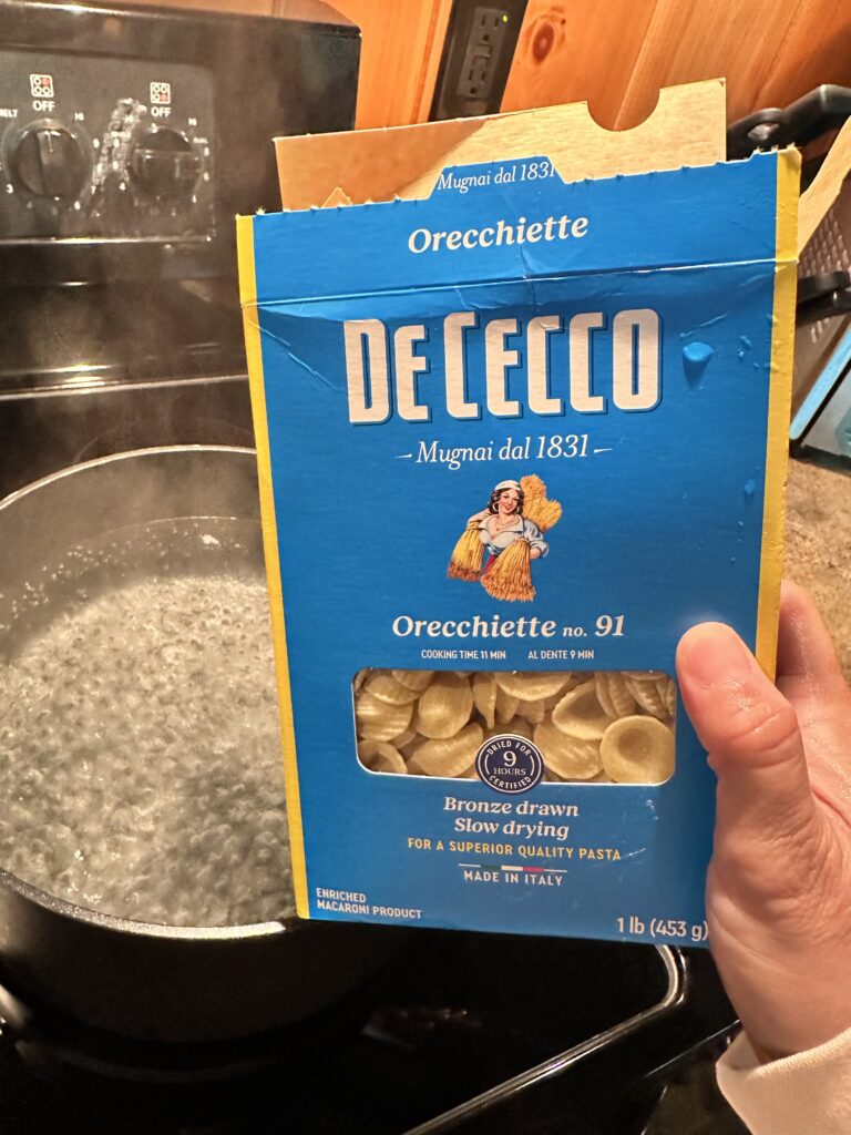 A box of orecchiette pasta in front of a pot of boiling water