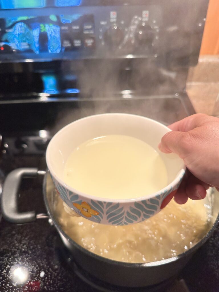 A bowl of pasta water held above a pot of boiling pasta
