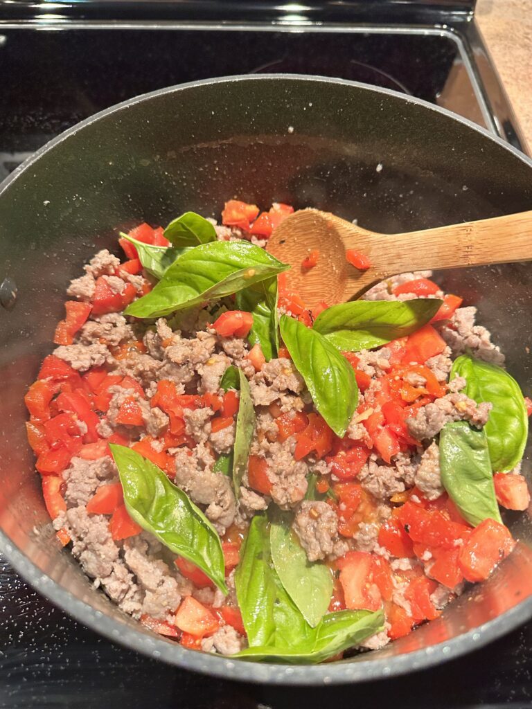 Crumbled sausage, diced pepper, and basil cooking in a pan