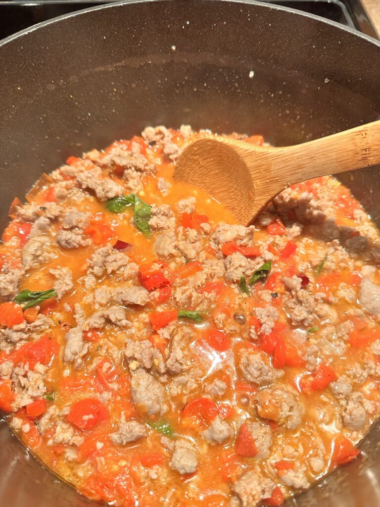 Sausage, diced pepper, and basil cooking in sauce