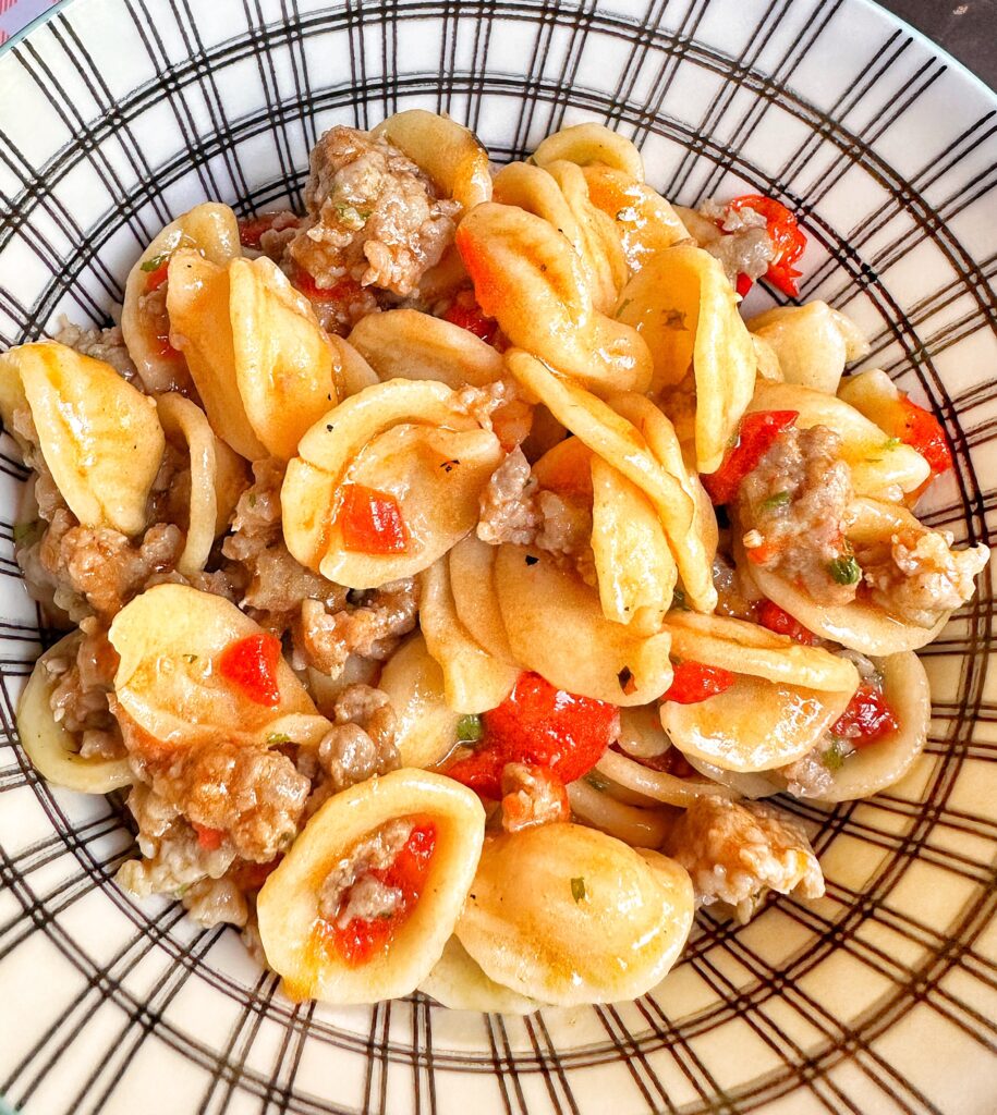 A bowl of orecchiette pasta with pepper and sausage seen from above