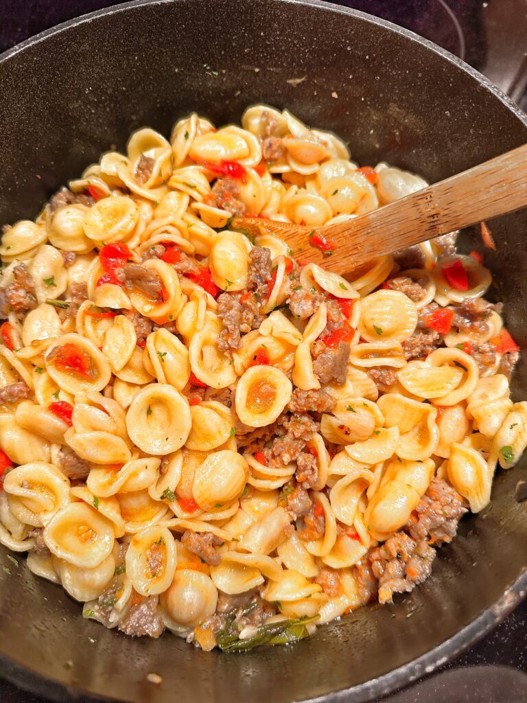 Orecchiette pasta with sausage and pepper in a pot with a wooden ladle