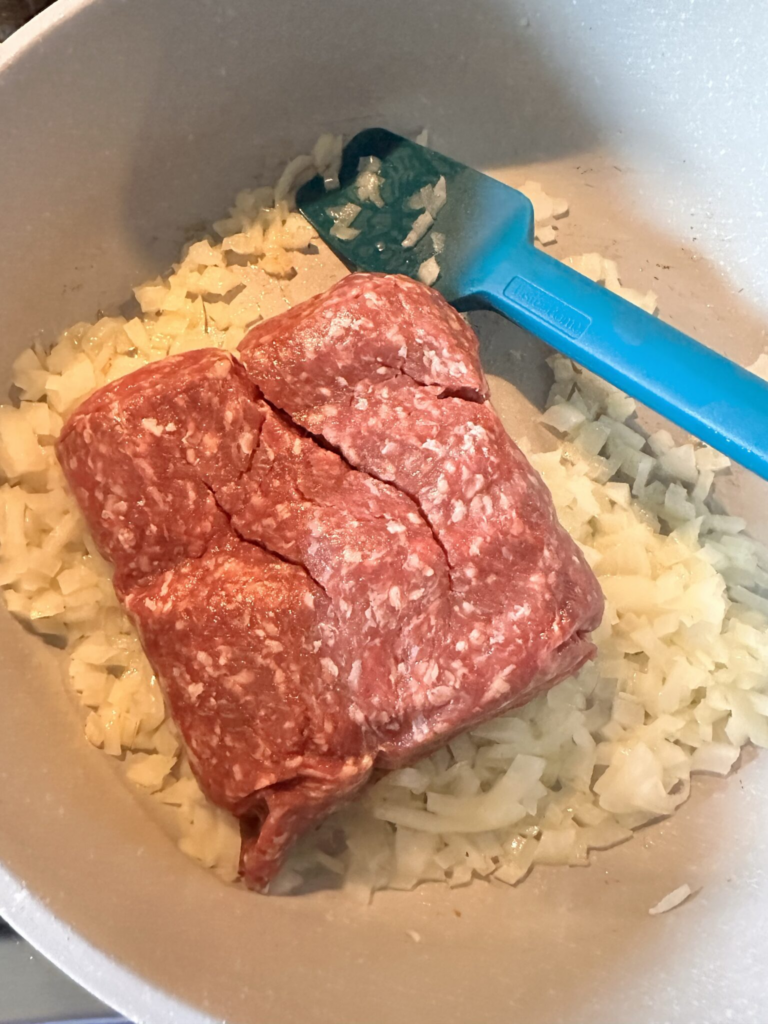 Raw ground beef in a pan with diced onions
