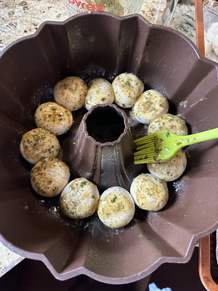 Uncooked rolls being brushed with butter and seasoning in a bundt pan