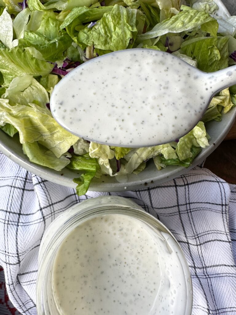 White salad dressing with seasoning in a spoon over a salad