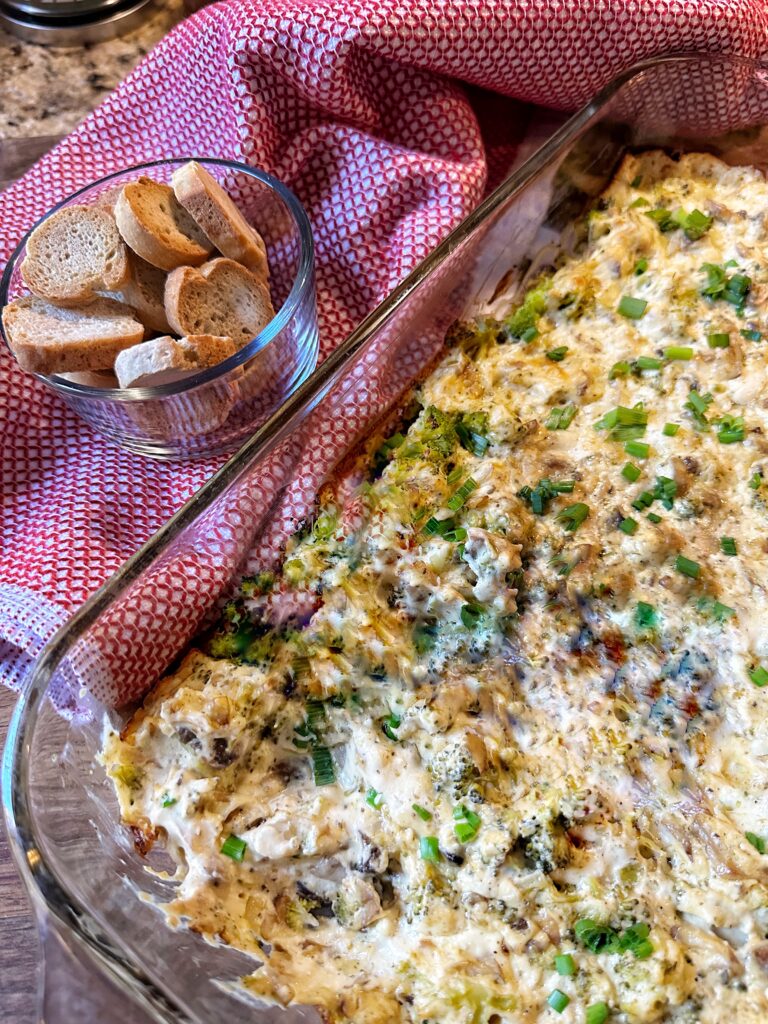 The finished dip topped with chives next to a small glass cup of crackers