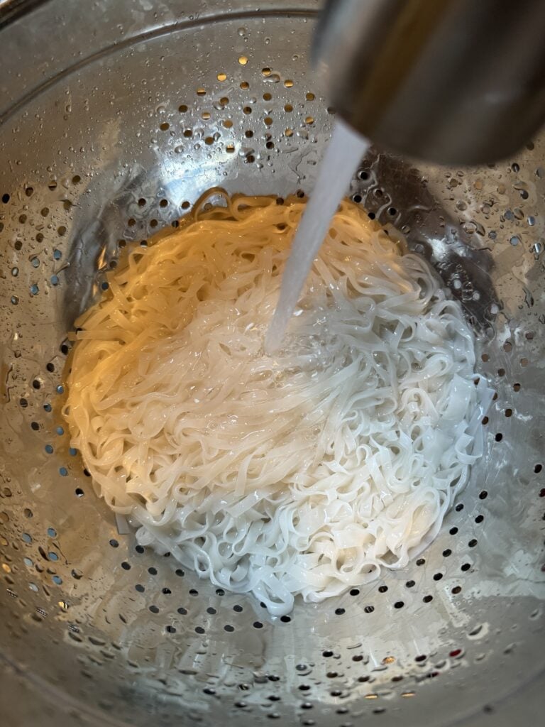 The rice noodles being rinsed in a strainer