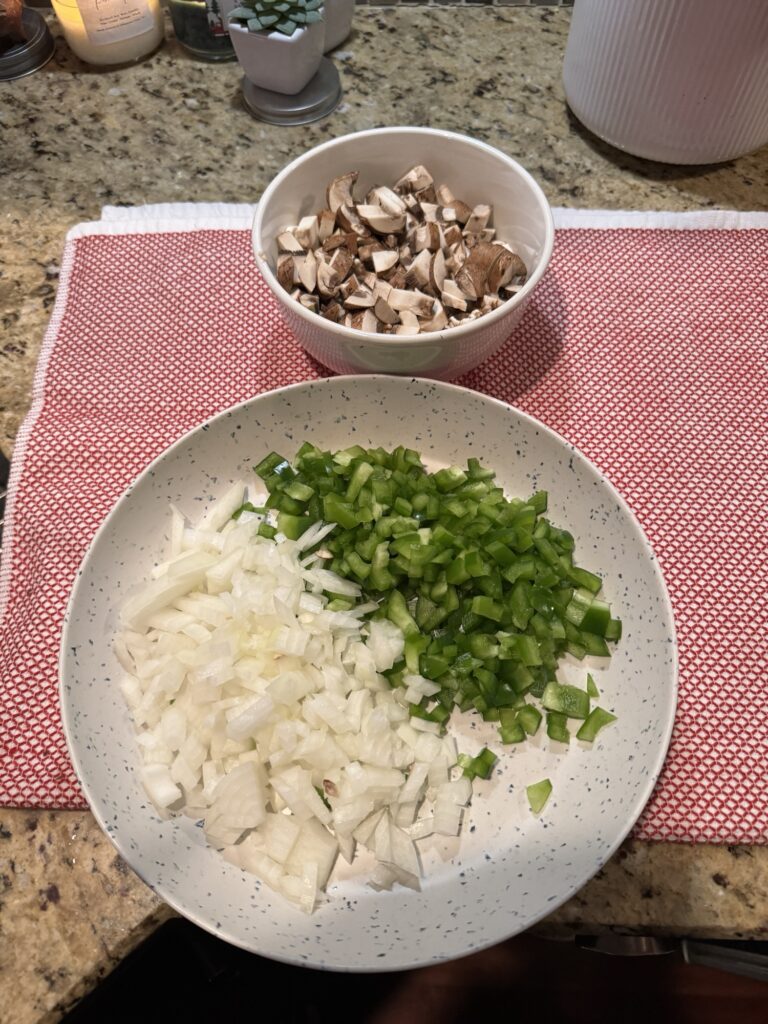 A small bowl of mushrooms and a plate of sliced green peppers and onion