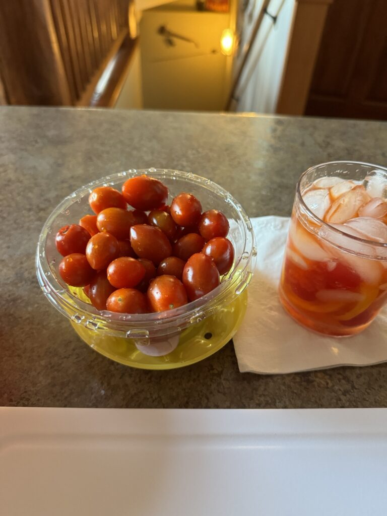 A small container of grape tomatoes next to a glass of red juice with ice in it