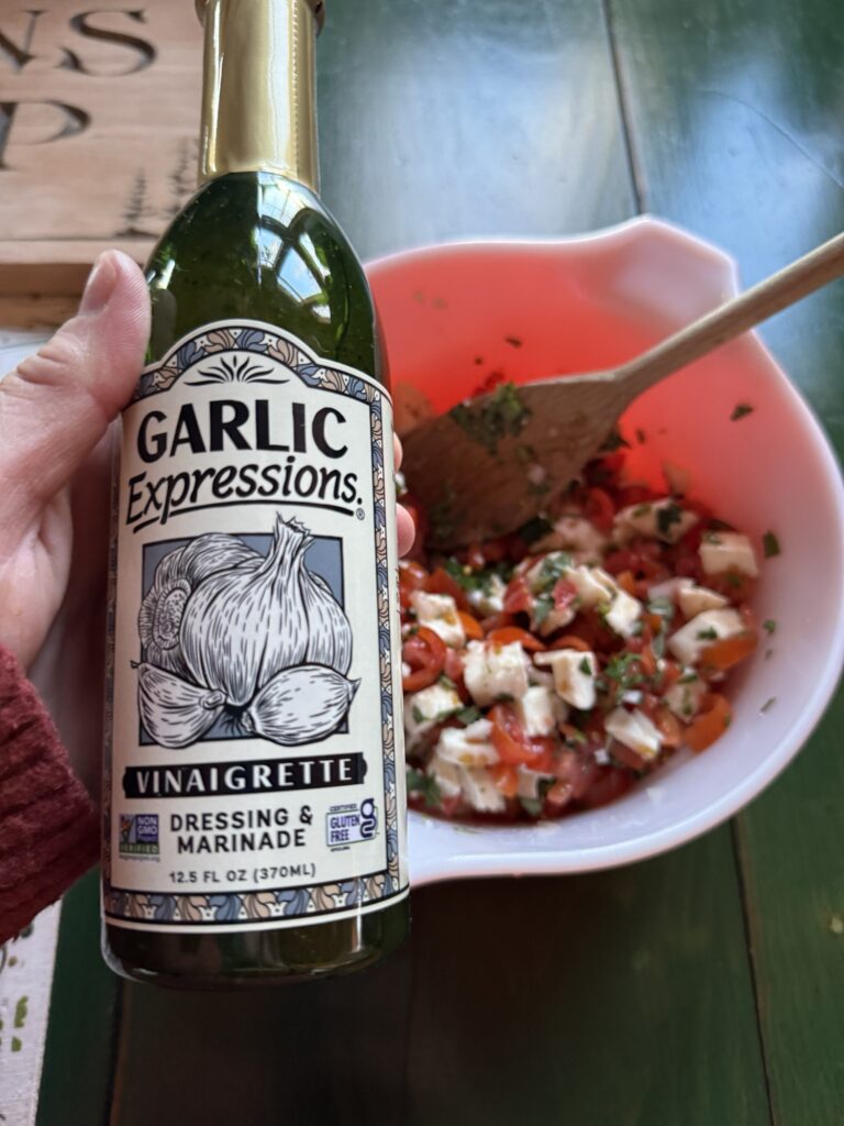A bottle of Garlic Expressions brand vinaigrette dressing being held over the bowl of bruschetta mix