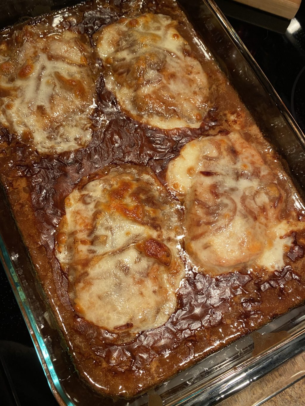 Baking dish with a brown onion gravy with boneless thick cut pork chops smothered in a white provolone cheese.