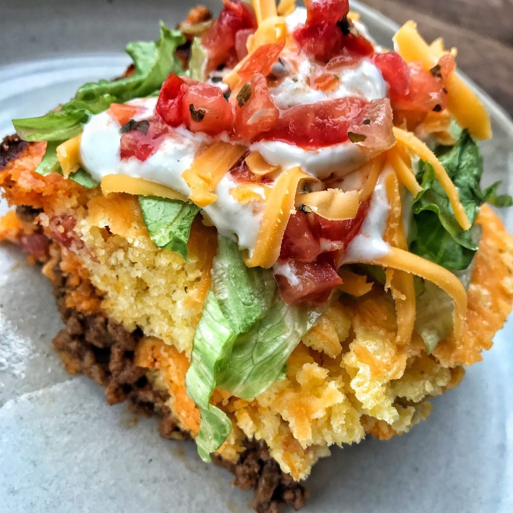 Taco Fixings on top of corn brad, ground beef, cheddar cheese shreds, sour cream and salsa