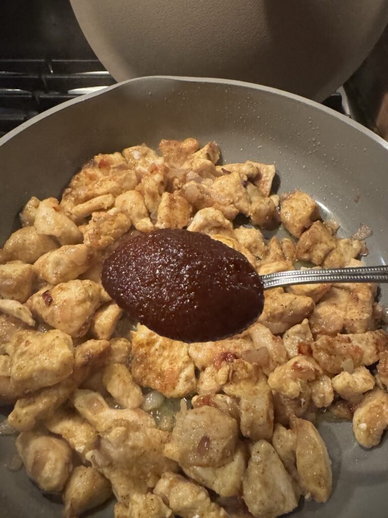 A spoonful of bouillon over chicken cooking in a pan