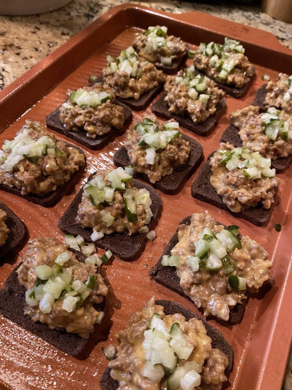 Rye toasts with meat mixture and pickle topping before baking
