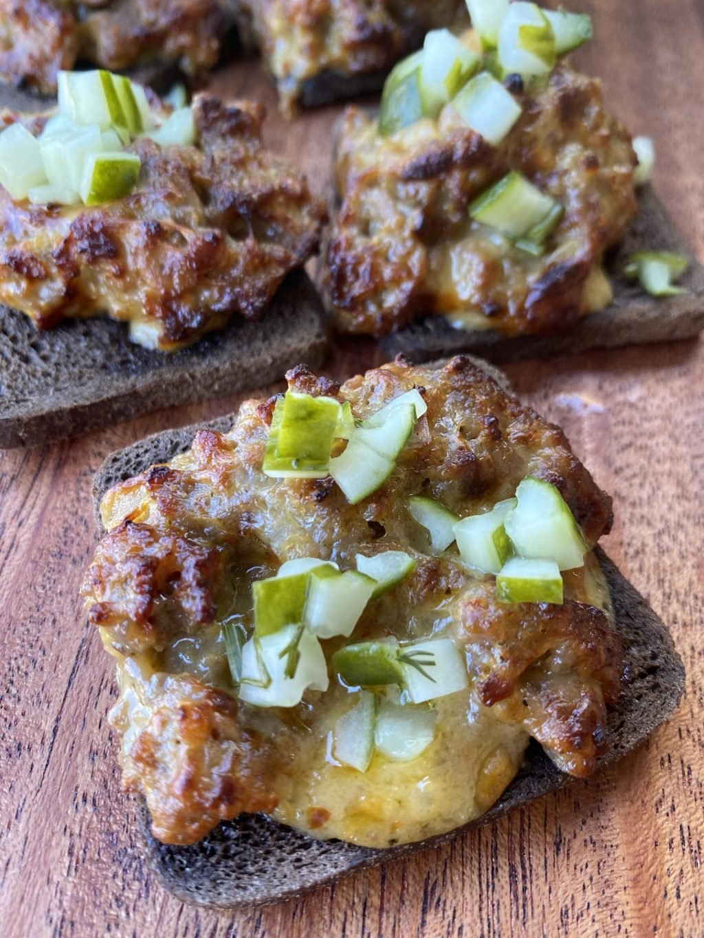 Mini rye bread slices with ground pork sausage crumbled on top, velveeta cheese melted in with onions and pickles