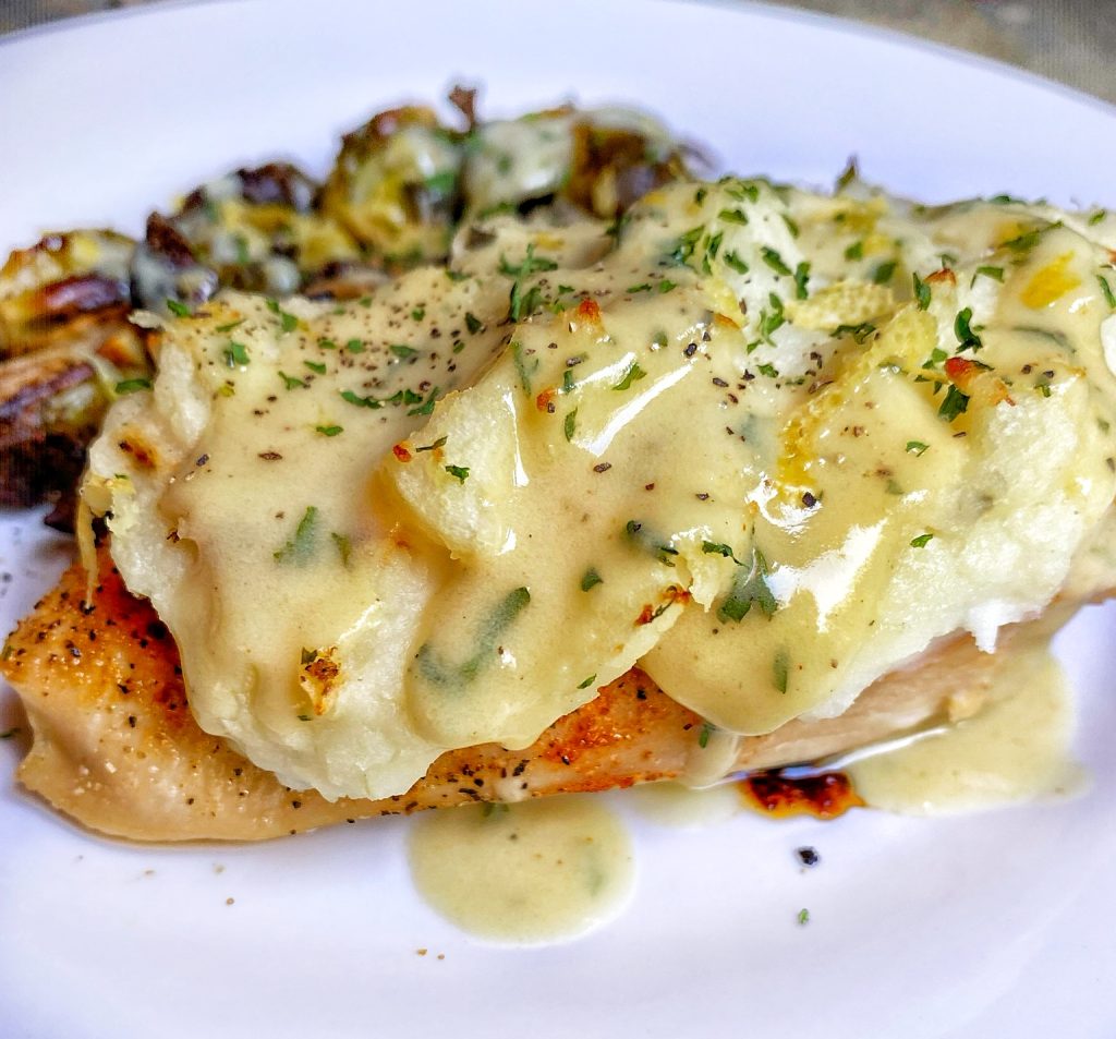 a chicken breast that has been baked and topped with mashed potatoes and then covered in a creamy béarnaise sauce