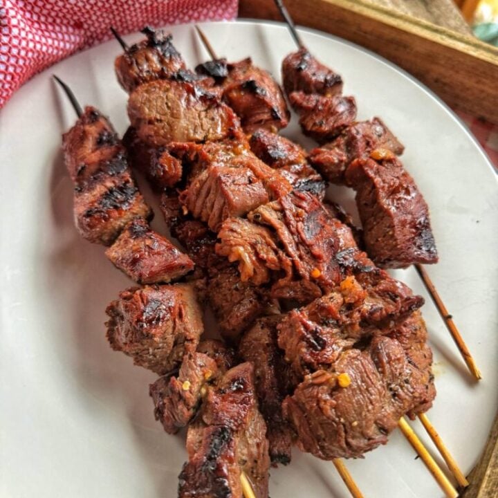 A white plate with 6 to 8 short wooden skewers on it with marinated beef tenderloin chunks