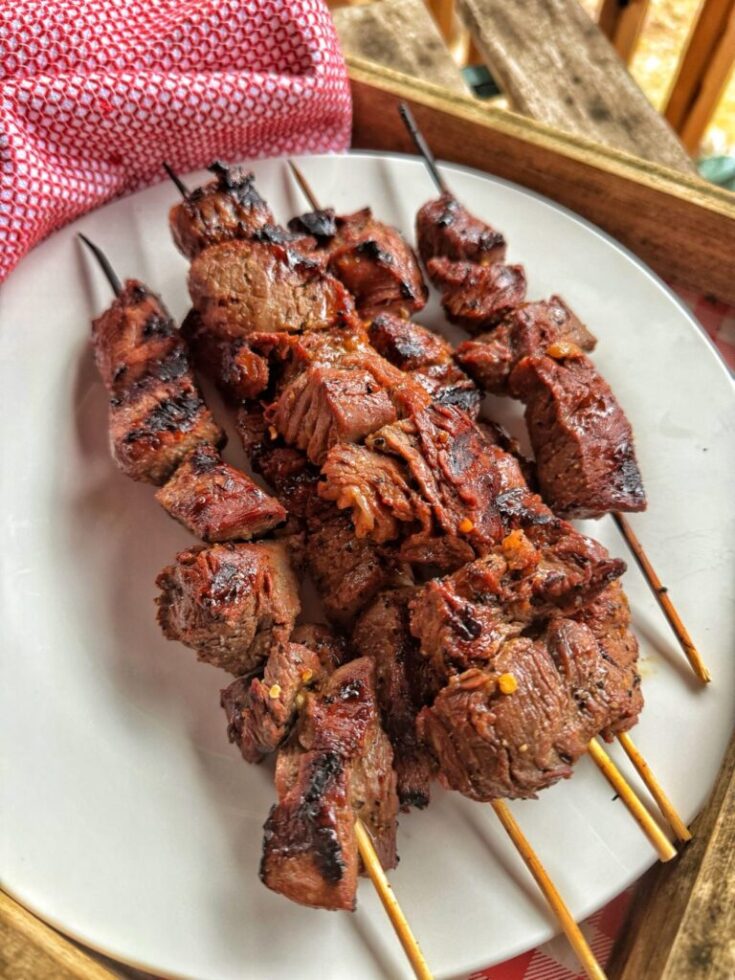 A white plate with 6 to 8 short wooden skewers on it with marinated beef tenderloin chunks