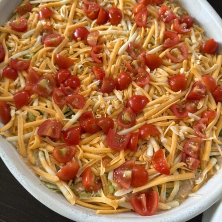 Platter of shredded orange and white taco cheese, tomatoes cut into quarters on top of sour cream, beans and guacamole.