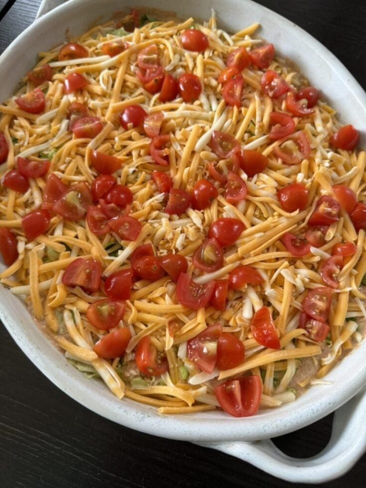 Platter of shredded orange and white taco cheese, tomatoes cut into quarters on top of sour cream, beans and guacamole.