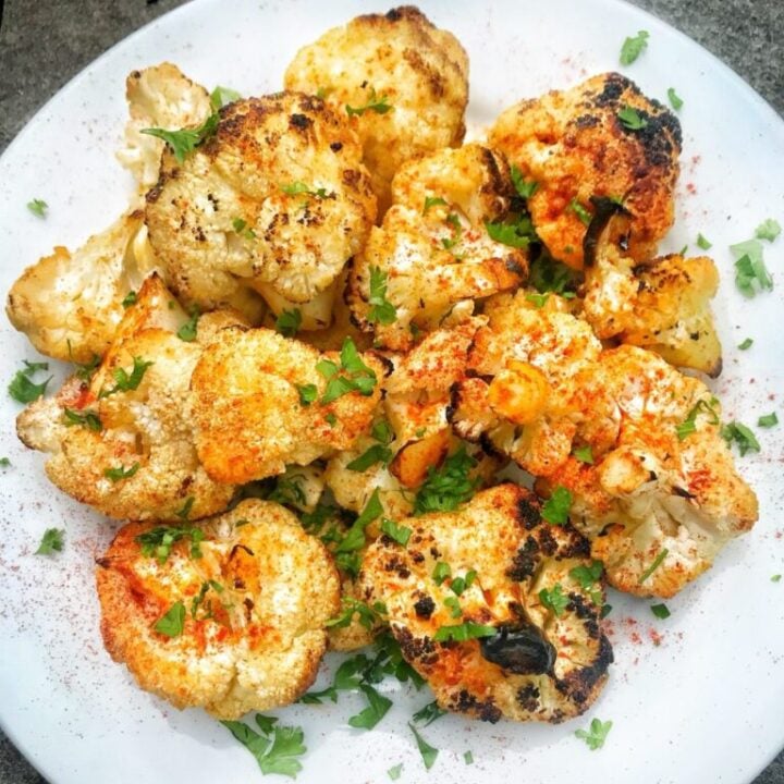 a white plate with cauliflower florets grilled with red paprika and green onions