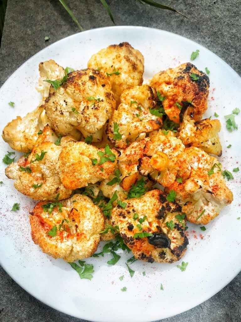 a white plate with cauliflower florets grilled with red paprika and green onions