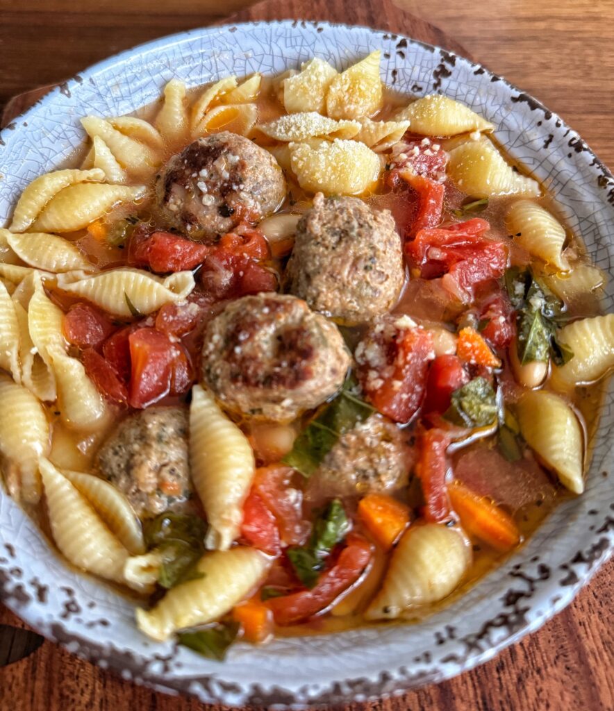 A close up shot of the finished meatball and vegetable soup with pasta shells in a bowl