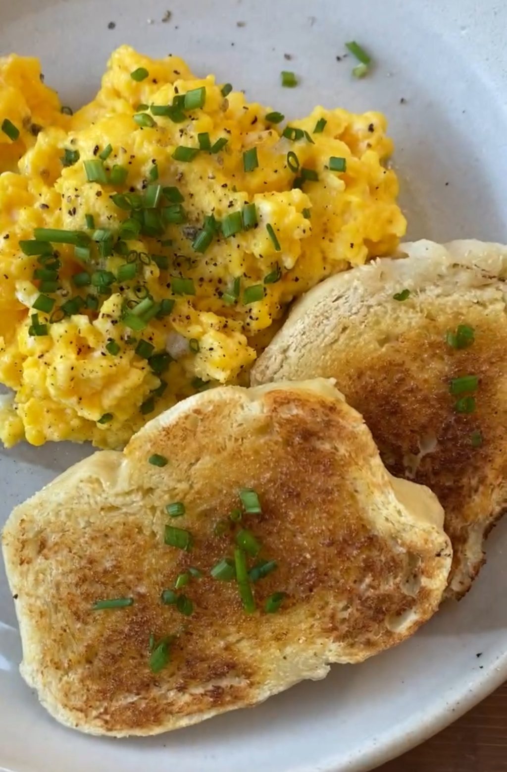 Scrambled eggs topped with chopped green onion on a plate next to two slices of toast