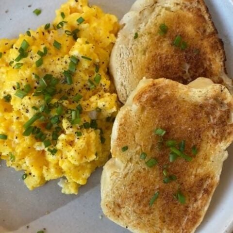 plate of fluffy, yellow scrambled eggs with green chives and two pieces of buttered french brad toasted