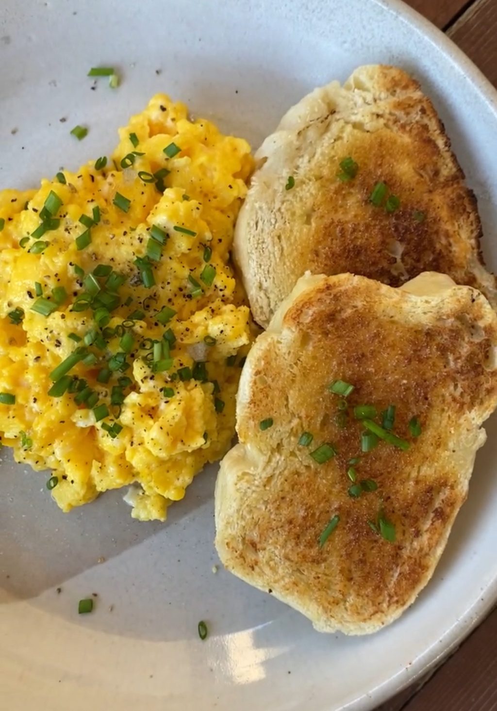 plate of fluffy, yellow scrambled eggs with green chives and two pieces of buttered french brad toasted