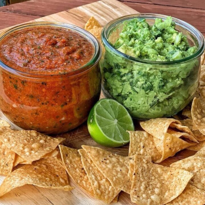 2 jars of salsa and guacamole with homemade chips on a wooden cutting board.