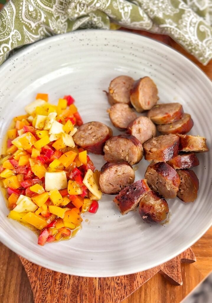 Plate with red, orange and yellow peppers salad with a side of grilled Italian sausage