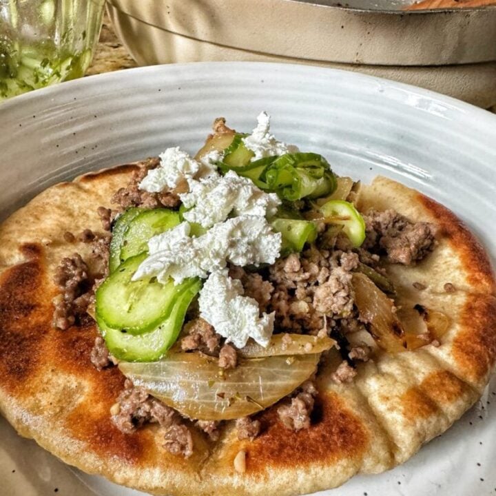 gray plate with a toasted pita bread, savory ground beef crumble, peppers and onions and a marinated cucumber salad topped with white feta cheese