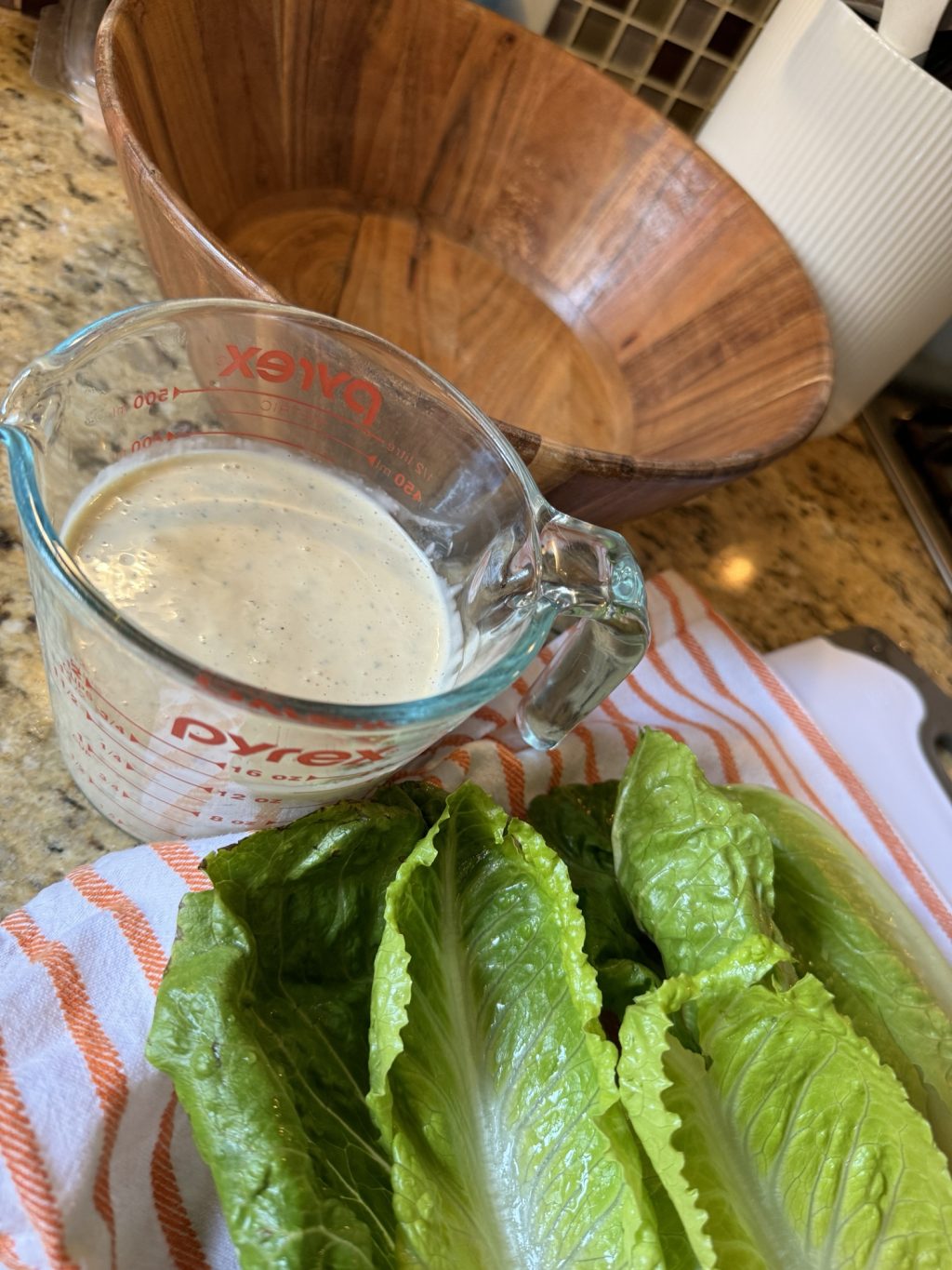 Caesar dressing in a Pyrex measuring cup next to a leaves of lettuce on a kitchen towel
