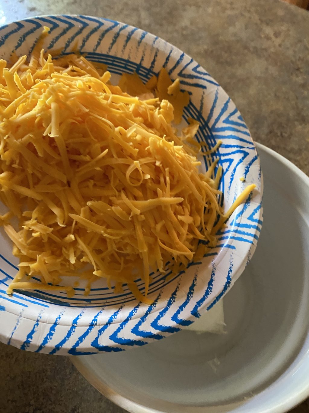 A paper bowl filled with shredded cheddar cheese