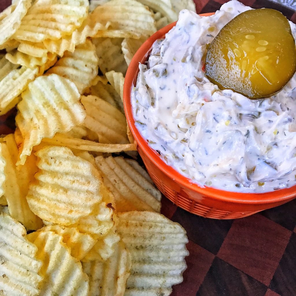 Chips next to a small red cup of white dip with a pickle chip on top