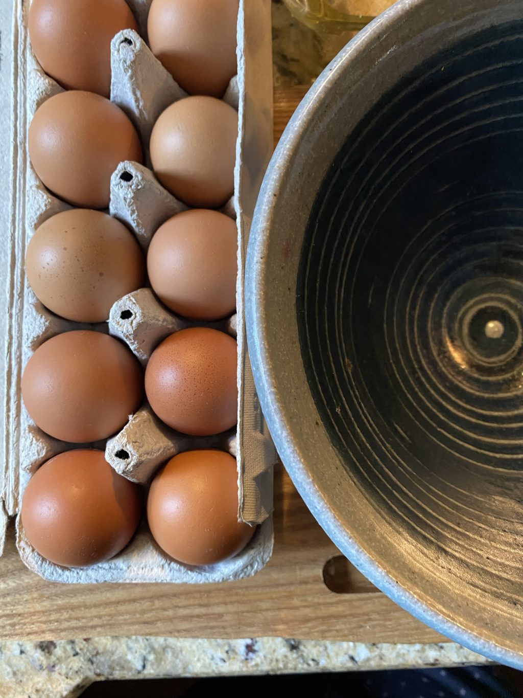 An open carton of eggs next to a ceramic bowl