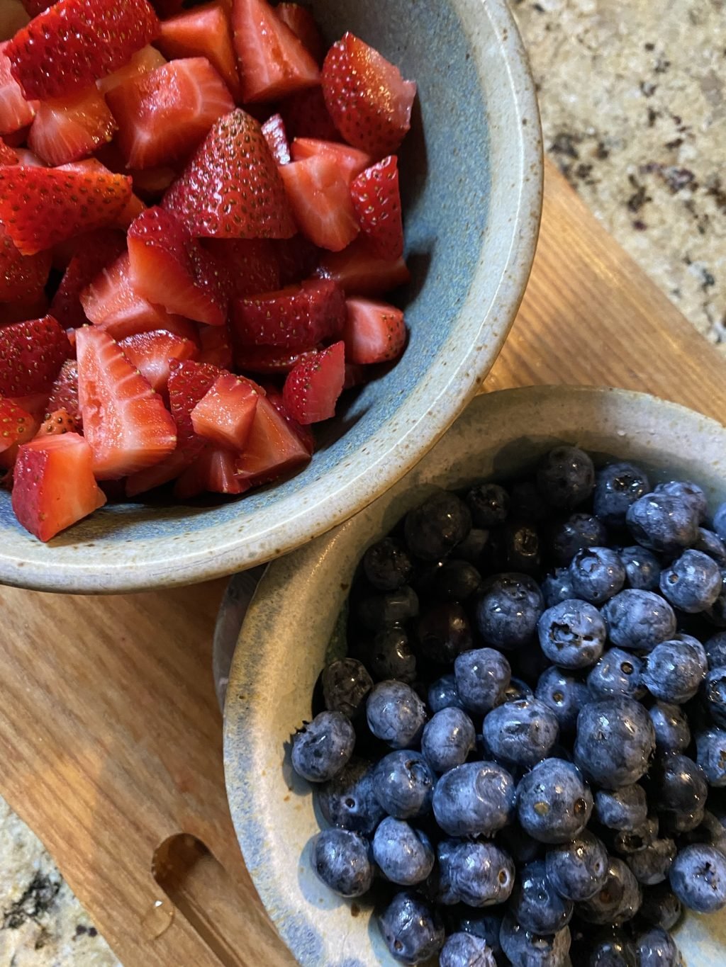 A bowl of cut strawberries and a bowl of blueberries