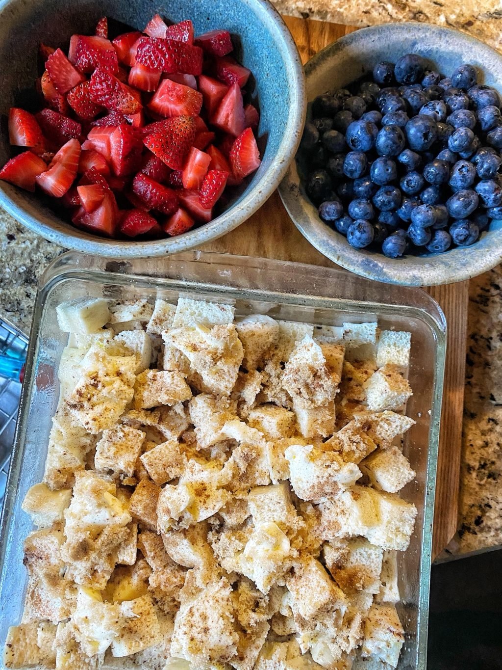 A bowl of strawberries, a bowl of blueberries, and a square glass baking dish with cubed pieces of bread
