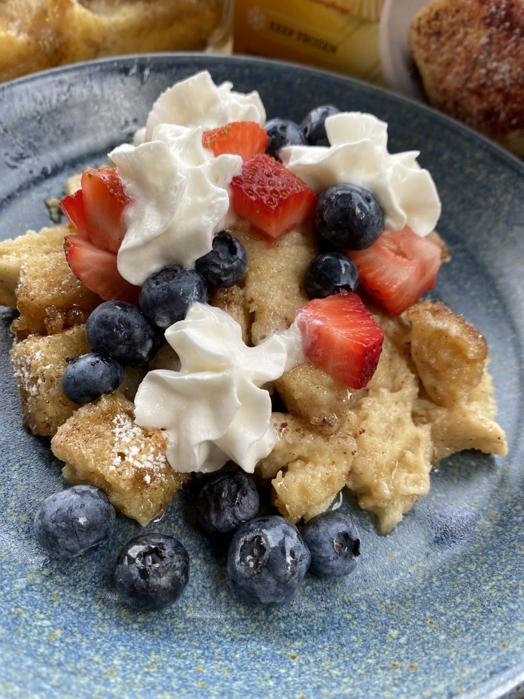 Cubes of French toast bake topped with cut strawberries, blueberries, and whipped cream
